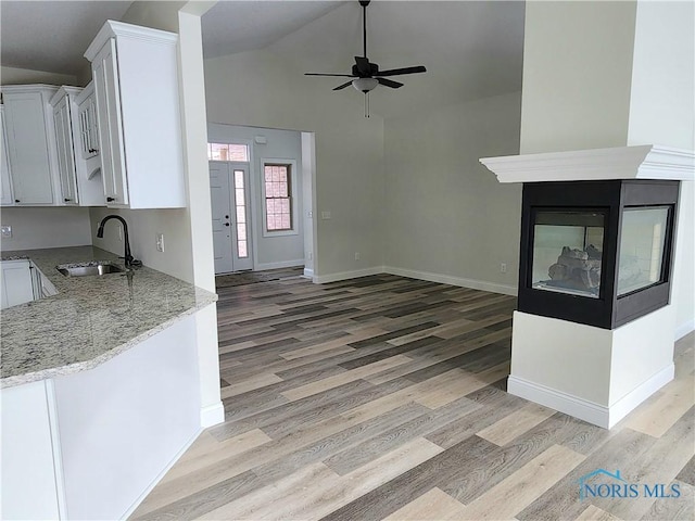 kitchen with light wood-type flooring, light stone countertops, vaulted ceiling, white cabinets, and sink