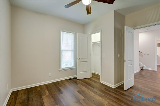 unfurnished bedroom featuring ceiling fan, dark wood-type flooring, a closet, and a walk in closet