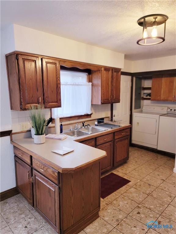 kitchen featuring kitchen peninsula, washing machine and clothes dryer, backsplash, and sink