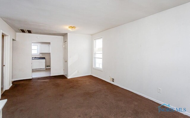 empty room featuring baseboards, visible vents, and dark carpet