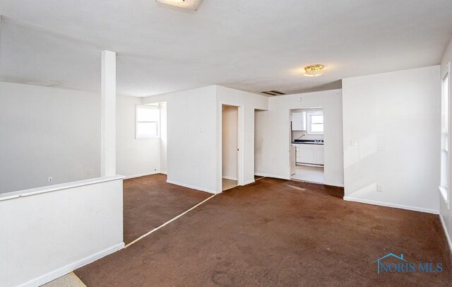 spare room featuring dark carpet, a wealth of natural light, and baseboards