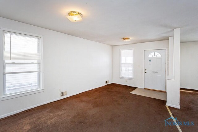 foyer entrance featuring dark colored carpet, visible vents, and baseboards