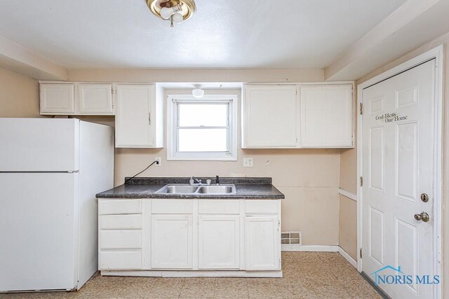 kitchen with freestanding refrigerator, white cabinets, a sink, and dark countertops