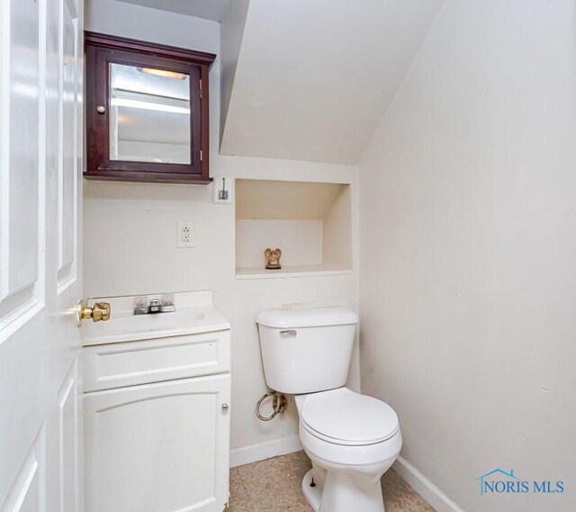 half bathroom with baseboards, vanity, and toilet