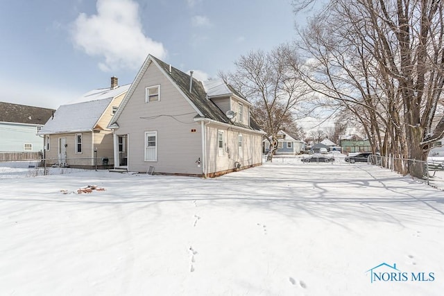 snow covered rear of property with entry steps and fence