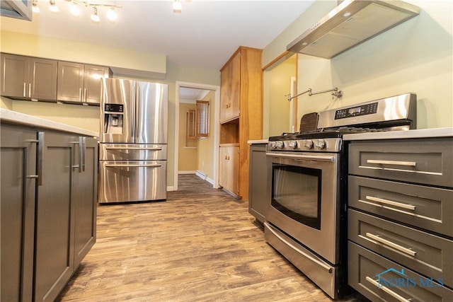 kitchen with gray cabinetry, stainless steel appliances, light wood-type flooring, and wall chimney range hood