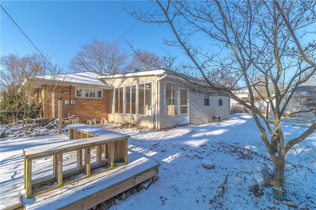 snow covered rear of property with a sunroom