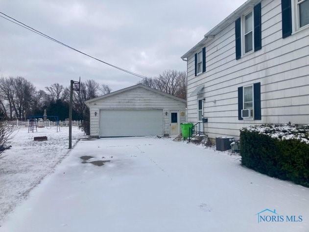 view of snow covered exterior featuring a garage and an outbuilding