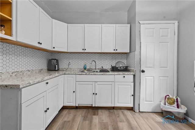 kitchen with light stone counters, decorative backsplash, light wood-type flooring, white cabinets, and sink