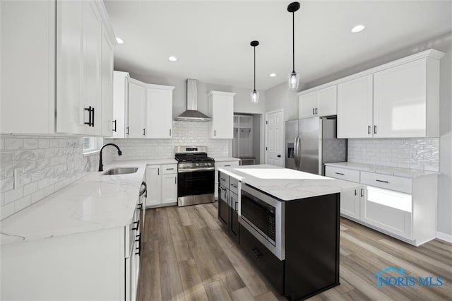 kitchen featuring hanging light fixtures, a center island, wall chimney range hood, white cabinets, and appliances with stainless steel finishes