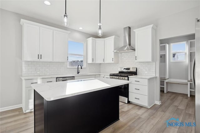 kitchen with appliances with stainless steel finishes, a kitchen island, white cabinetry, and wall chimney exhaust hood