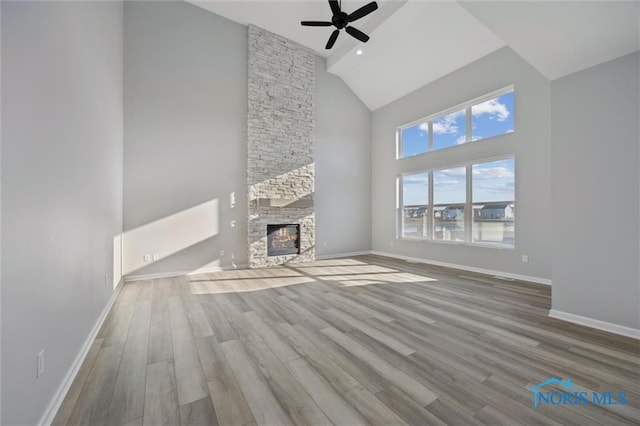 unfurnished living room featuring ceiling fan, a stone fireplace, high vaulted ceiling, and hardwood / wood-style flooring