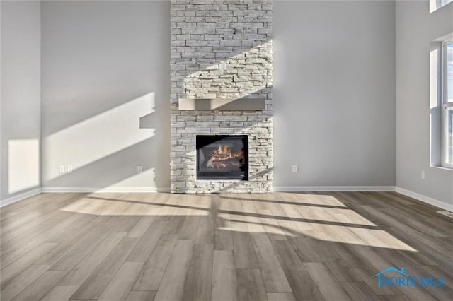 unfurnished living room with hardwood / wood-style flooring and a stone fireplace