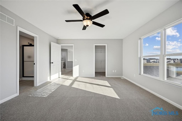 unfurnished bedroom with a closet, light carpet, a water view, ceiling fan, and a walk in closet