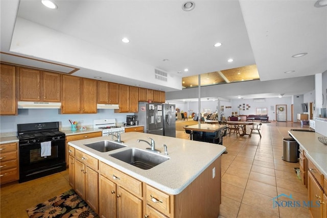 kitchen featuring black range with gas cooktop, stainless steel fridge with ice dispenser, sink, and a center island with sink