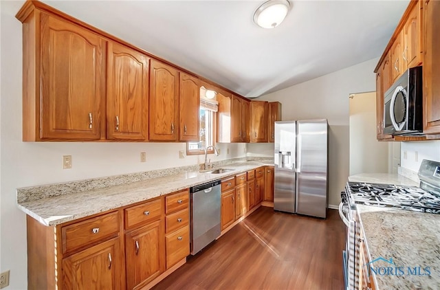 kitchen featuring light stone counters, vaulted ceiling, dark hardwood / wood-style floors, appliances with stainless steel finishes, and sink