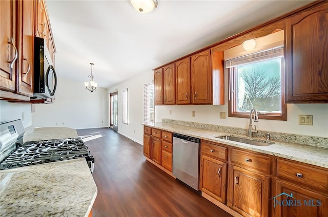 kitchen with stainless steel appliances, hanging light fixtures, a notable chandelier, light stone counters, and sink