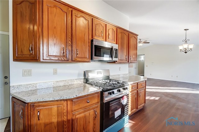 kitchen with light stone counters, dark wood-type flooring, decorative light fixtures, ceiling fan with notable chandelier, and appliances with stainless steel finishes