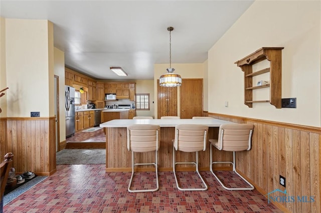 kitchen featuring a kitchen bar, hanging light fixtures, stainless steel refrigerator, wooden walls, and kitchen peninsula