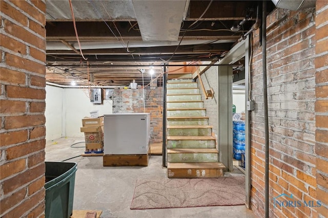 basement featuring electric panel, brick wall, and refrigerator