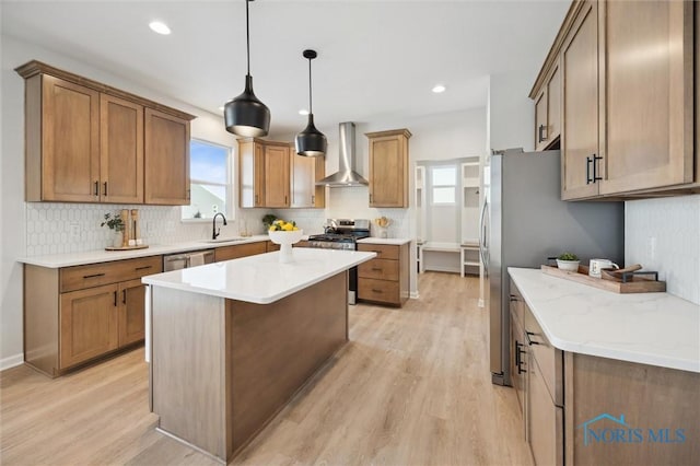 kitchen featuring stainless steel appliances, light wood-type flooring, wall chimney exhaust hood, sink, and decorative light fixtures