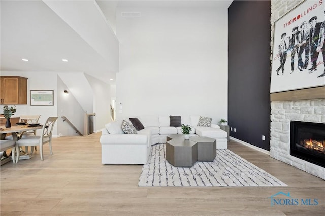 living room featuring visible vents, a towering ceiling, a stone fireplace, light wood-type flooring, and recessed lighting