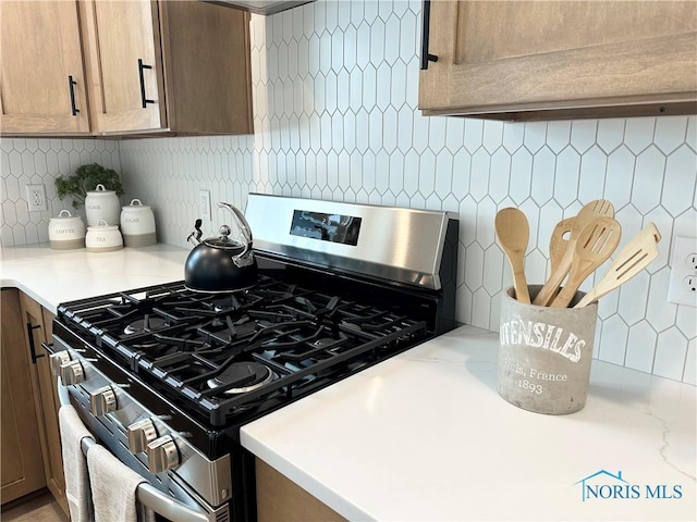 kitchen featuring light countertops, backsplash, and gas range