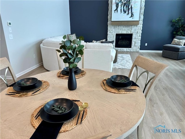 dining space with a stone fireplace, baseboards, and wood finished floors