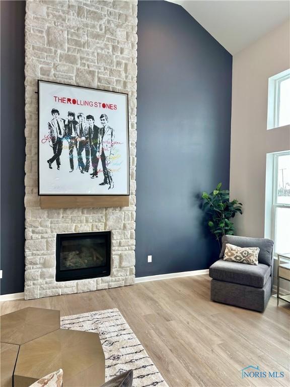 living area with high vaulted ceiling, a stone fireplace, baseboards, and wood finished floors