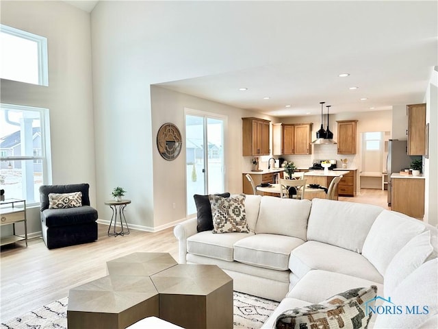 living room featuring baseboards, light wood finished floors, recessed lighting, and a healthy amount of sunlight