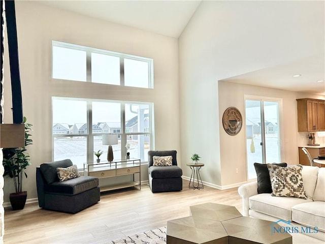 living room with light wood-style floors, high vaulted ceiling, and baseboards