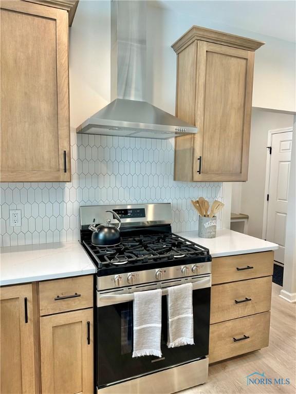 kitchen featuring stainless steel gas stove, tasteful backsplash, light countertops, light brown cabinetry, and wall chimney range hood