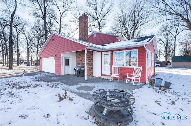 snow covered back of property with a garage