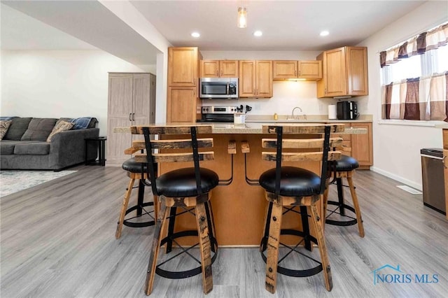 kitchen with appliances with stainless steel finishes, a kitchen island, light brown cabinets, light hardwood / wood-style floors, and a breakfast bar area