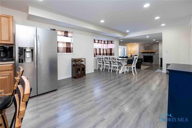 kitchen featuring light brown cabinets, stainless steel fridge, light hardwood / wood-style flooring, and a fireplace