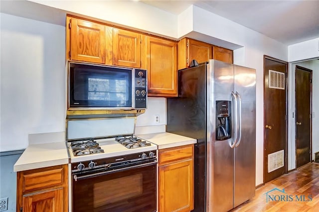 kitchen featuring white range with gas stovetop, stainless steel fridge, and light wood-type flooring