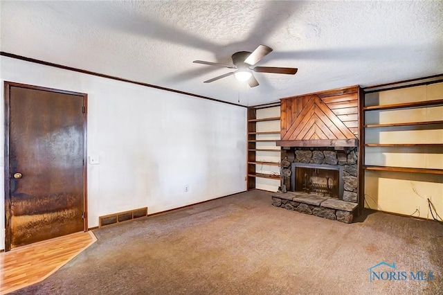 unfurnished living room with ceiling fan, a textured ceiling, carpet floors, and a stone fireplace