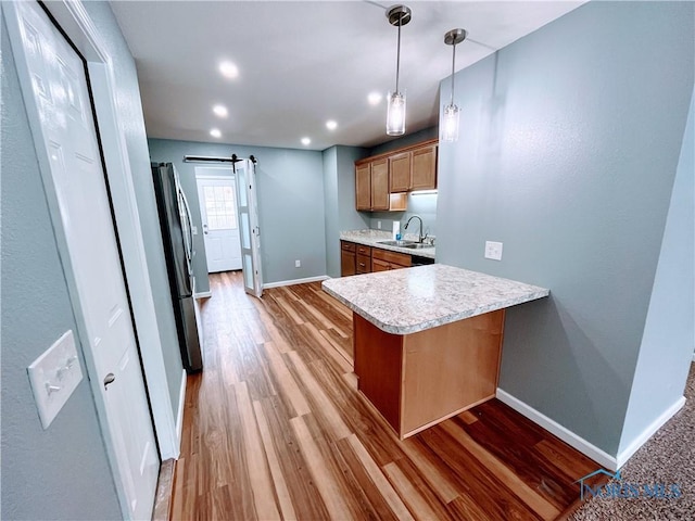 kitchen featuring decorative light fixtures, sink, light hardwood / wood-style floors, kitchen peninsula, and a barn door