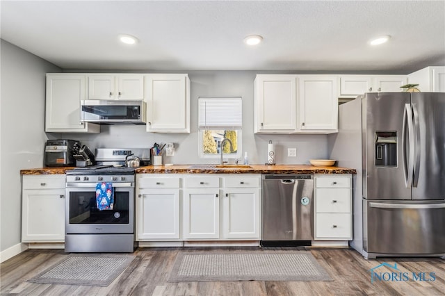 kitchen with dark wood-type flooring, appliances with stainless steel finishes, white cabinets, and sink