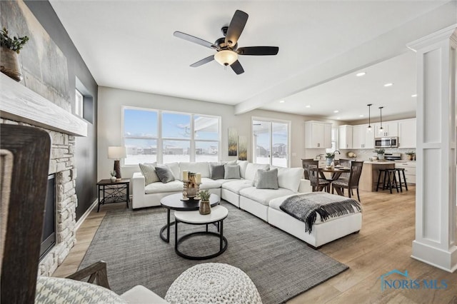 living room featuring ceiling fan, beam ceiling, light wood-type flooring, and a fireplace