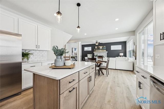 kitchen featuring stainless steel appliances, pendant lighting, white cabinets, light stone counters, and a center island