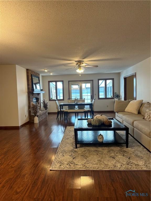 living room featuring ceiling fan, a fireplace, a textured ceiling, and dark wood-type flooring