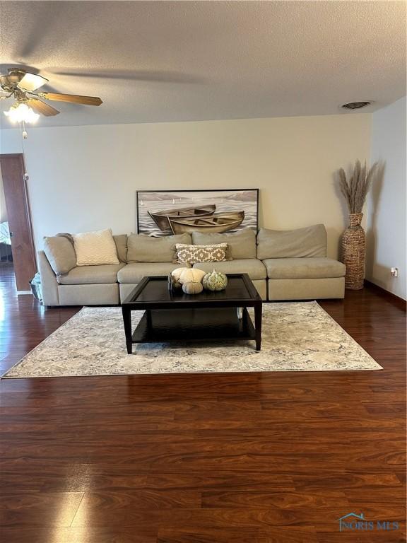 living room featuring ceiling fan, dark wood-type flooring, and a textured ceiling