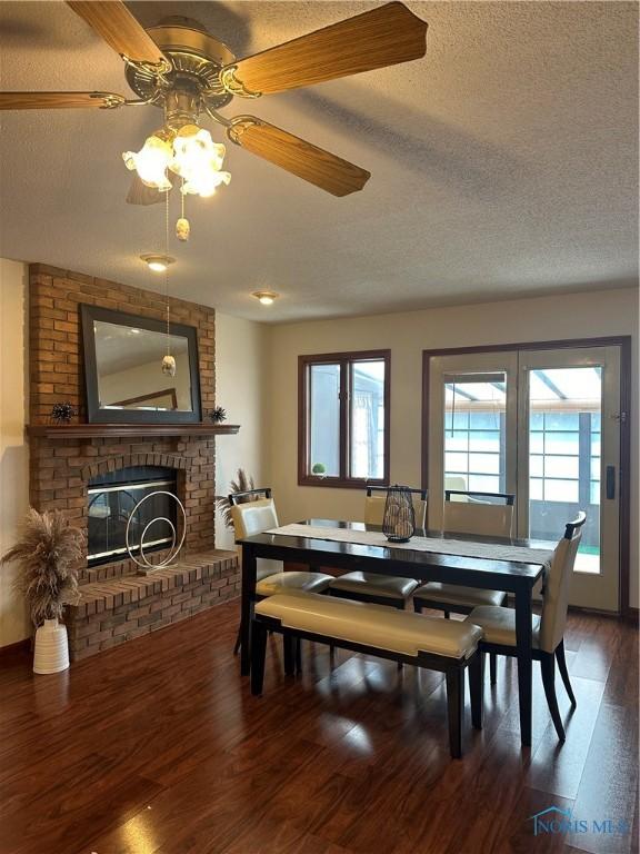 dining room featuring a textured ceiling, a brick fireplace, hardwood / wood-style flooring, and ceiling fan