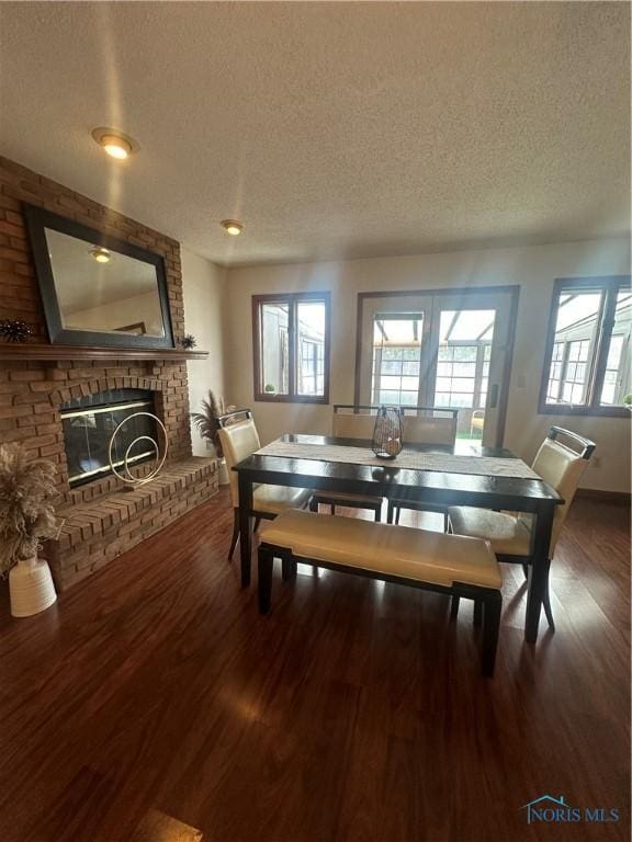 dining room featuring wood-type flooring, a brick fireplace, a wealth of natural light, and a textured ceiling