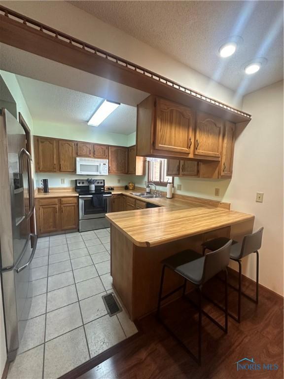 kitchen featuring a textured ceiling, appliances with stainless steel finishes, a kitchen bar, kitchen peninsula, and light tile patterned flooring