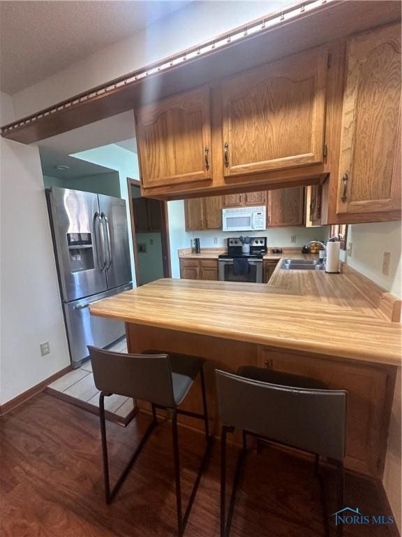 kitchen featuring wood counters, kitchen peninsula, appliances with stainless steel finishes, light hardwood / wood-style flooring, and sink