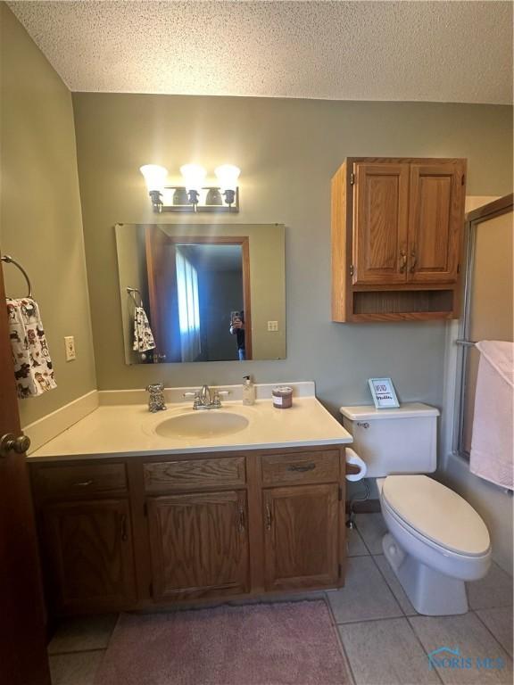 bathroom featuring a textured ceiling, tile patterned floors, vanity, toilet, and a shower with shower door