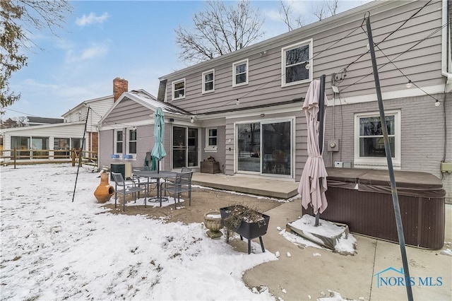 snow covered house featuring a patio area and a hot tub