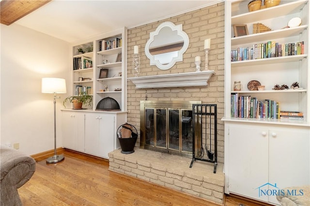 living room featuring built in features, a brick fireplace, and light hardwood / wood-style floors